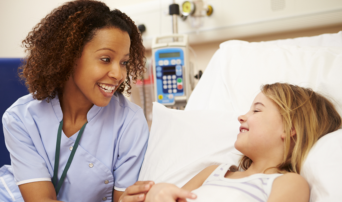 Female nurse sitting next to a child in a hospital bed.