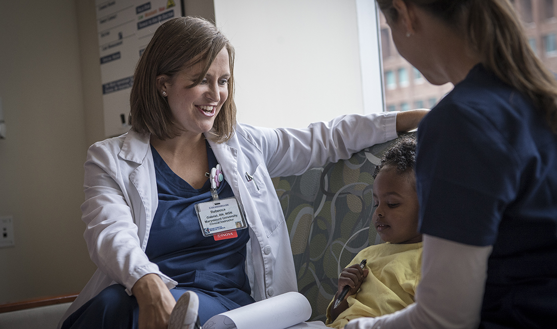 Two female nurses sitting on a sofa next to a child.